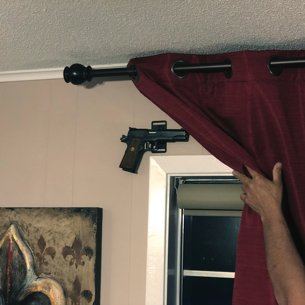 CoJo gun magnet holding over a window behind a curtain in a house.